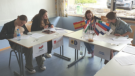 Vier Jugendliche arbeiten an einem Tisch, auf dem Flaggen europäischer Länder stehen.