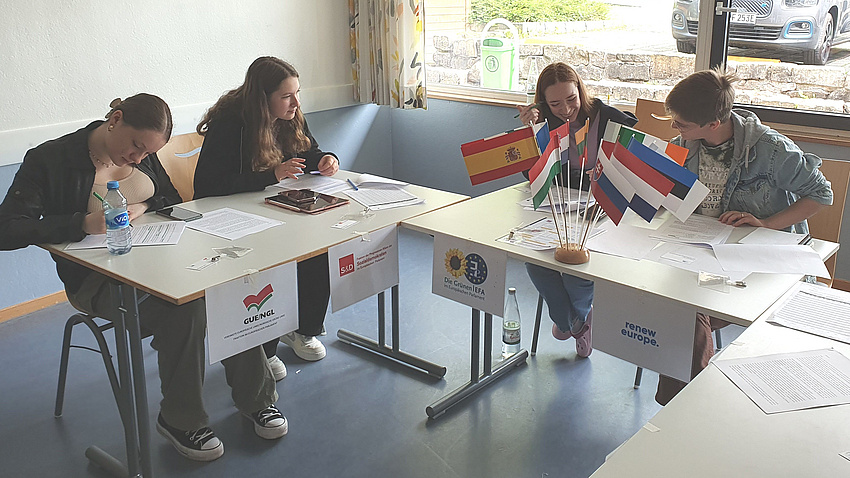 Vier Jugendliche arbeiten an einem Tisch, auf dem Flaggen europäischer Länder stehen.