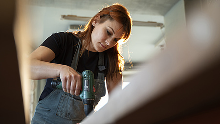 Eine Frau bohrt mit der Bohrmaschine in ein Holzbrett