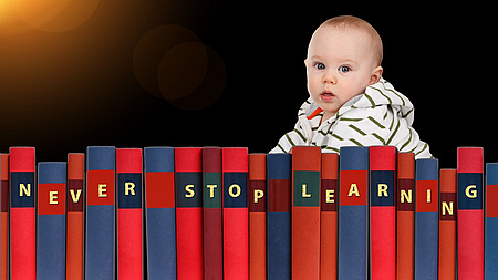 Baby hinter Buchrücken mit dem Schriftzug NEVER STOP LEARNING
