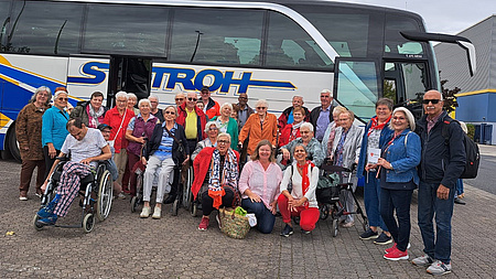 Eine große Gruppe von Seniorinnen und Senioren steht vor einem Reisebus.