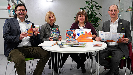 Kjetil Dahlhaus, Stephanie Roser, Sabine Coldehoff und Jan Weckler sitzen an einem Tisch. Sie zeigen Flyer und Plakate.
