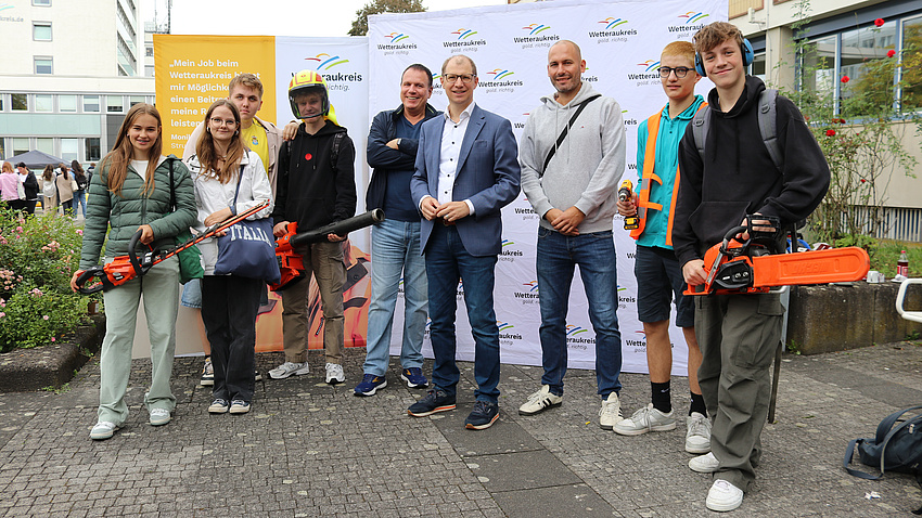 Landrat Jan Weckler steht mit Schülern und Lehrern auf dem Europaplatz. Die Schüler halten Arbeitsgeräte in der Hand und lächeln.