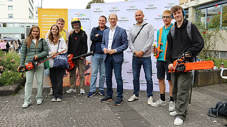 Landrat Jan Weckler steht mit Schülern und Lehrern auf dem Europaplatz. Die Schüler halten Arbeitsgeräte in der Hand und lächeln.
