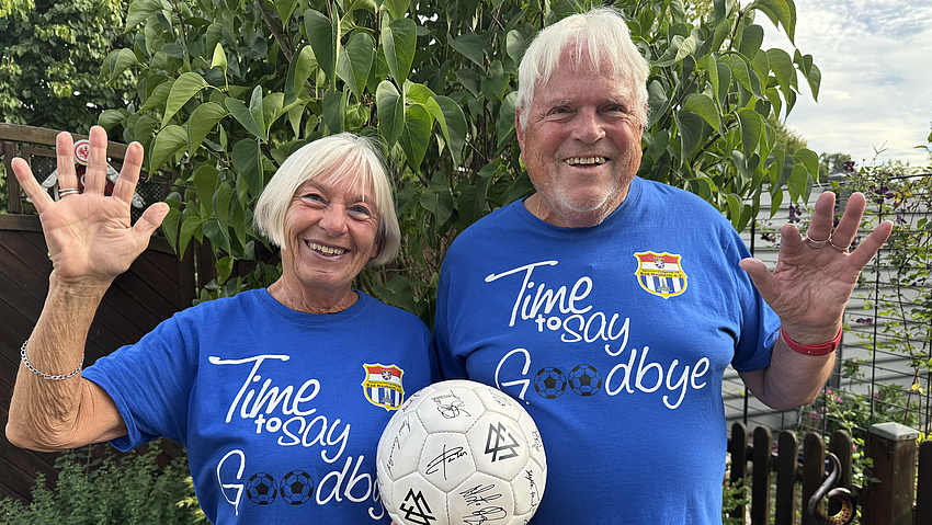 Ein älteres Ehepaar lächelt in die Kamera. Beide halten gemeinsam einen Fußball.