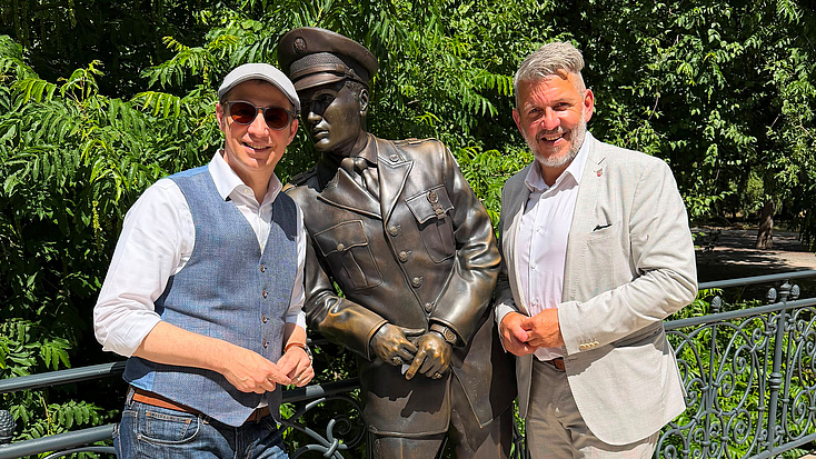 Zwei Personen stehen rechts und links neben einer Bronzestatur von Elvis Presley in Bad Nauheim. .