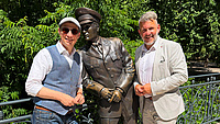 Zwei Personen stehen rechts und links neben einer Bronzestatur von Elvis Presley in Bad Nauheim. .