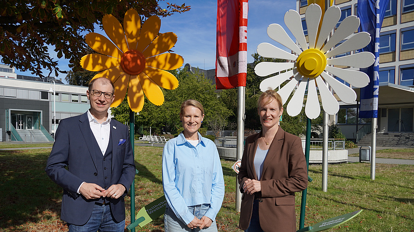 Das Foto zeigt Landrat Jan Weckler, LGS-Beauftragte Anne Kemink und Erste Kreisbeigeordnete Birgit Weckler vor den Holzblumen..