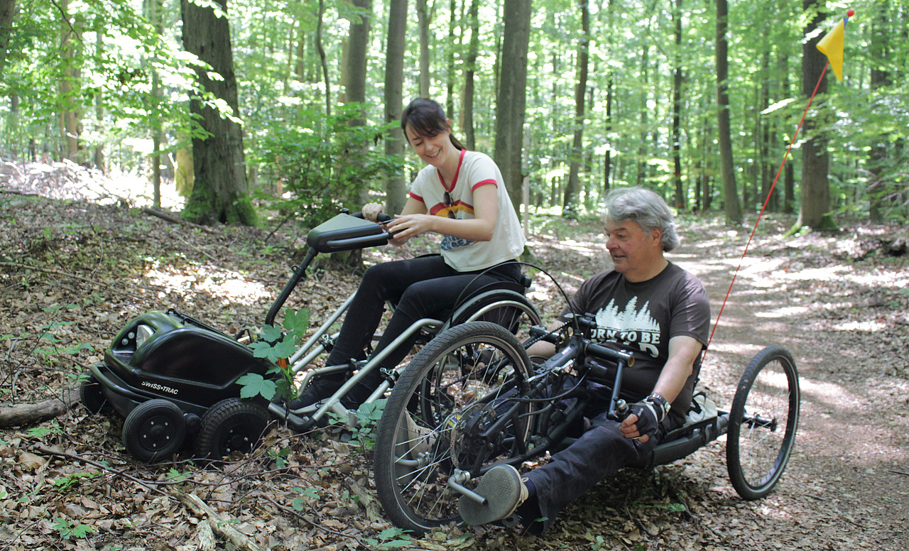 Eine Rollstuhlfahrerin und ein Rollstuhlfahrer im Wald