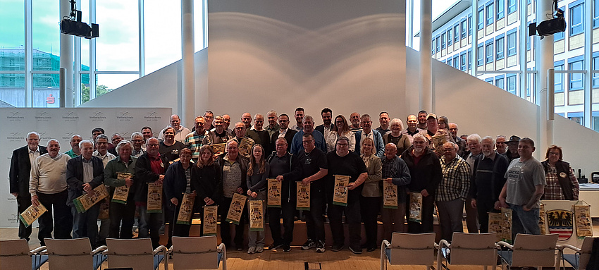Eine große Personengruppe steht in einem großen Saal. Viele der Abgebildeten halten Wimpel in Händen.