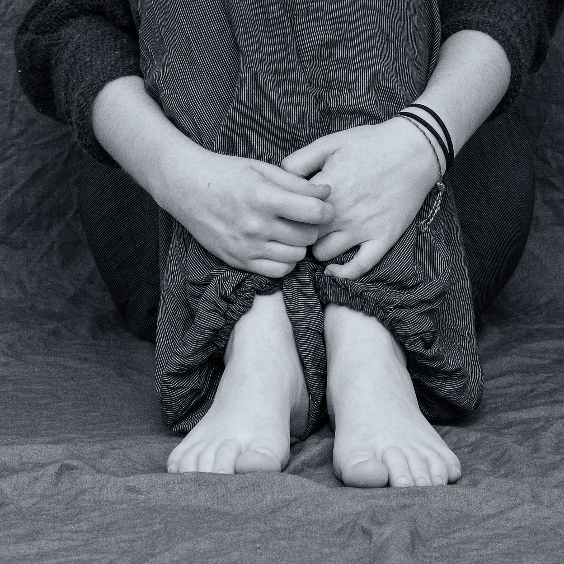 Sitzende Person, die die Arme um die Beine schlingt