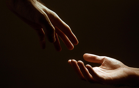 Eine Hand in helfender Geste zu einer aufgehaltenen Hand.