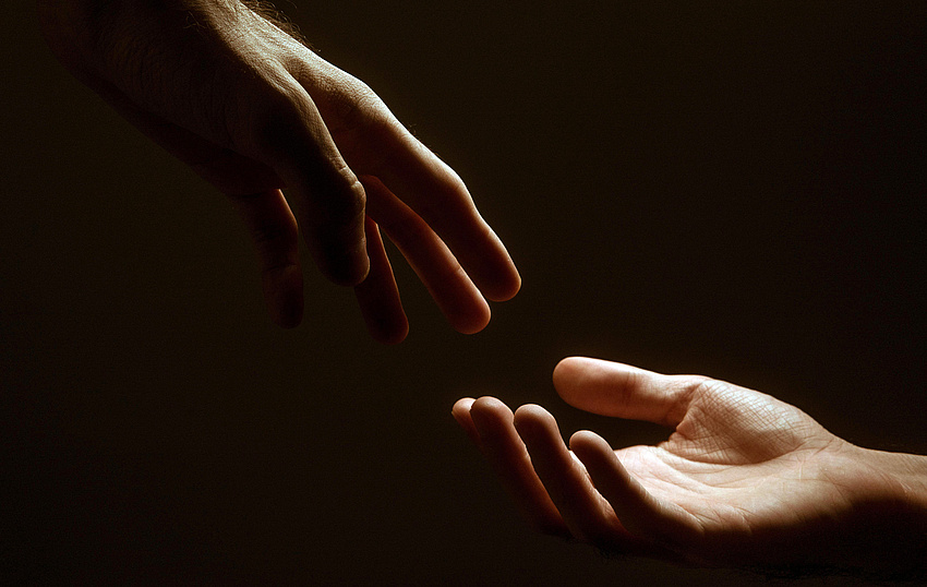 Eine Hand in helfender Geste zu einer aufgehaltenen Hand.