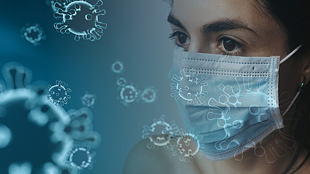Symbolfoto: Frau mit Maske neben einem übergroßen Virus