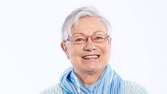 Ein ältere Frau mit kurzen grauen Haaren lacht in die Kamera