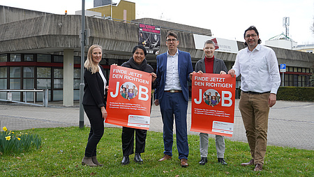 5 Menschen stehen auf einer Wiese und halten zwei Plakate.