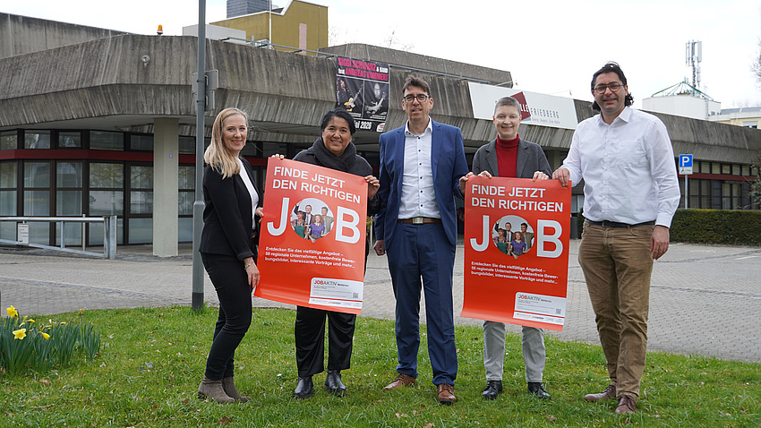 5 Menschen stehen auf einer Wiese und halten zwei Plakate.