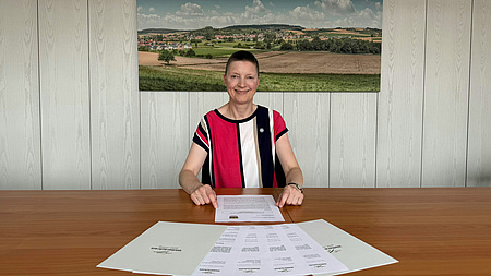 Eine Frau sitzt an einem großen Tisch, vor ihr liegen aufgefächert mehrere Blätter Papier.
