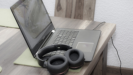 Ein aufgeklappter Laptop, auf der Tastatur liegt ein Kopfhörer
