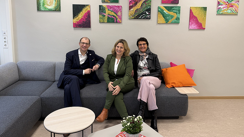 Drei Personen sitzen nebeneinander auf dem Sofa im neu gestalteten Lehrerzimmer der Georg-August-Zinn-Schule.