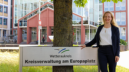 Eine Frau steht vor dem Gebäude der Kreisverwaltung. Sie lächelt in die Kamera.