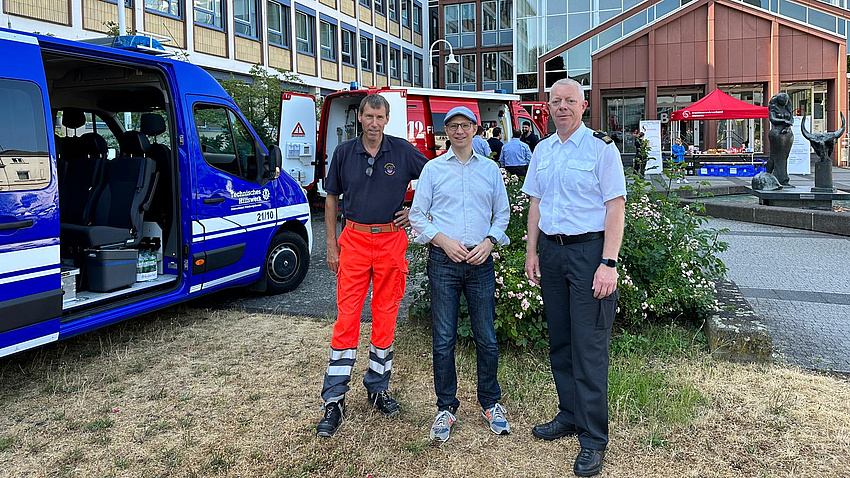 Landrat Jan Weckler und zwei weitere Männer in Uniform stehen vor einem blauen Einsatzfahrzeug.
