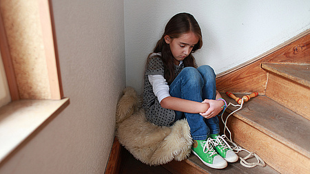 Ein trauriges Mädchen sitzt auf einer Treppe.