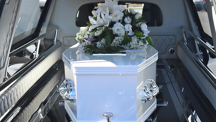 Ein Sarg mit Blumenstrauß in einem Leichenwagen.