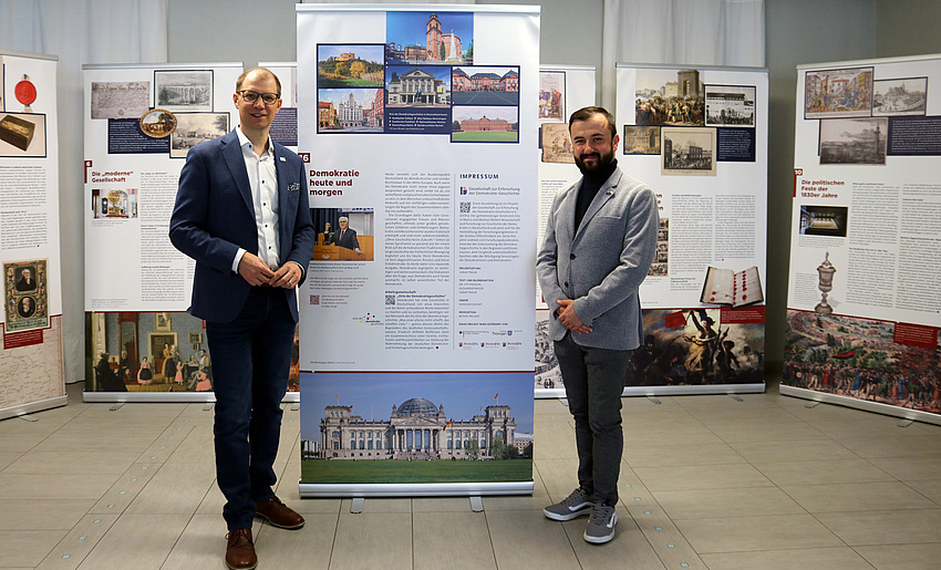 Zwei Männer stehen vor einigen Rollups, die im Halbkreis angeordnet sind.