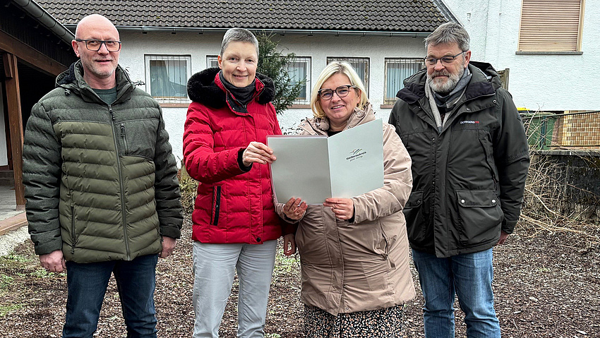 Vier Personen blicken in die Kamera und halten einen Förderbescheid in den Händen.