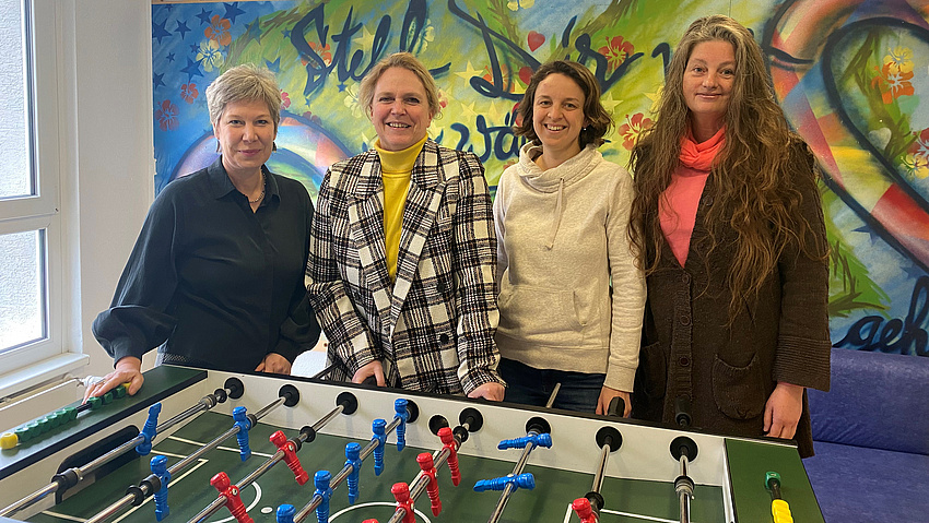Vier Frauen stehen an einem Tischkicker. Sie lächeln in die Kamera.
