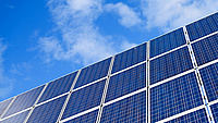 Mehrere Photovoltaik-Module zur Stromerzeugung sind vor einem blauen Himmel mit einigen Wolken zu sehen.
