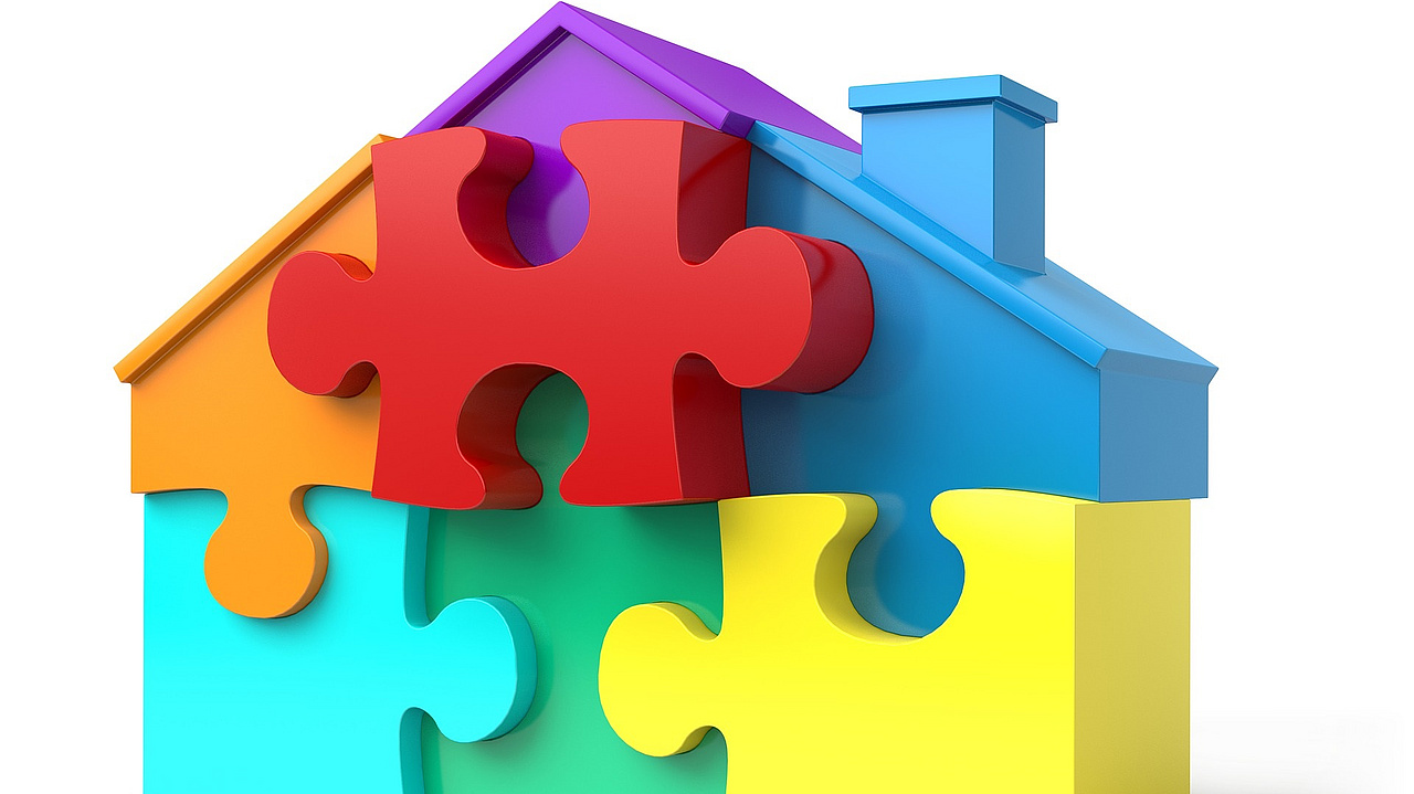 Ein Haus, das aus mehreren Puzzleteilen in kräftigen Farben besteht.