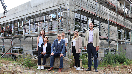 Eine kleine Gruppe von Leuten steht vor einem Rohbau mit Gerüst.