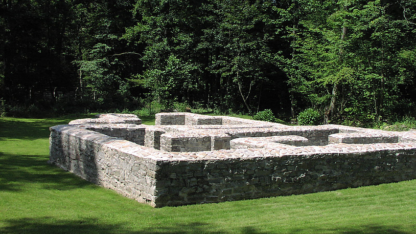 Grundmauern eines historischen Gebäudes. Im Hintergrund Bäume.