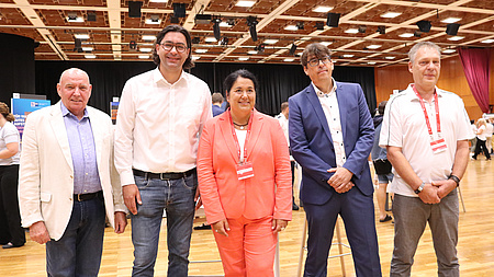 Fünf Menschen stehen in einer Messehalle.