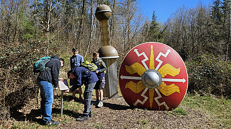 Mehrere Jungen stehen in einem Wald um ein Hinweisschild herum.