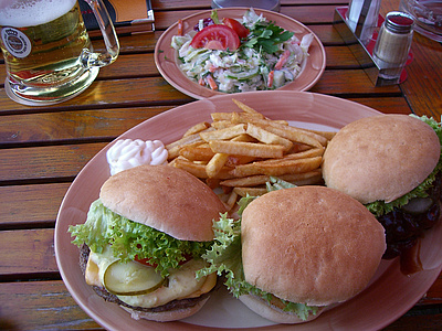 Kaum zu schaffen aber extrem lecker! Ein Teller mit 3 Hamburgern und Pommes, Salat und ein Glas Bier Vera Löwenberg/pixelio.de