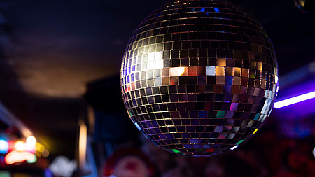 Eine Discokugel hängt vor einem verschwommenen Hintergrund mit bunten Lichtern.