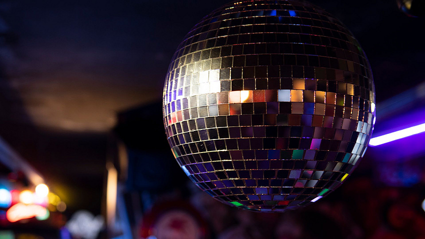 Eine Discokugel hängt vor einem verschwommenen Hintergrund mit bunten Lichtern.