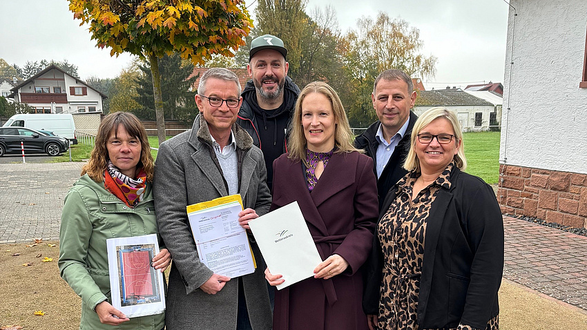 Mehrere Menschen stehen auf einem alten Sportplatz und halten verschiedene Zertifikate in die Kamera.