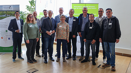 Eine Gruppe von Personen steht vor einem Banner. Die Männer und Frauen lächeln in die Kamera.