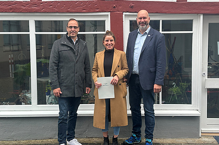 Eine Frau und zwei Männer stehen vor einem Fachwerkgebäude.