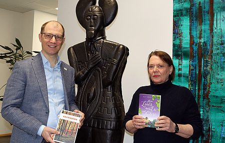 Ein Mann und eine Frau stehen neben der Statue des Keltenfürsten. Beide haben ein Buch in der Hand. Im Hintergrund ein abstraktes Gemälde.