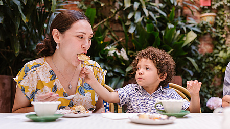 Ein Kind füttert seine Mutter mit einem Brötchen am Tisch