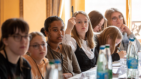 Mädchen sitzen am Tisch, eines meldet ich mit einem Stift