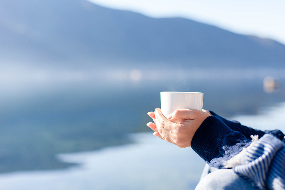 Eine Frau hält eine Tasse Tee in der Hand und blickt über einen See