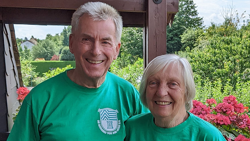 Helga und Wolfgang Lingenau in grünen Vereins-T-Shirts. Sie lächeln in die Kamera.
