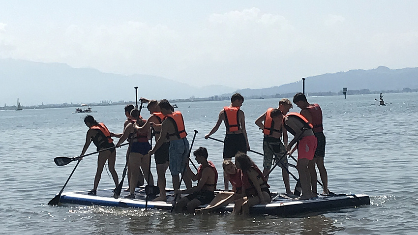 Jugendliche mit Schwimmwesten auf einem Floß auf dem See