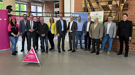 Dreizehn Männer und Frauen stehen vor einem pinken, dreieckigen Aufsteller. Darauf steht: "Glasfaser-Bauarbeiten."